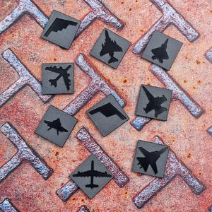 May include: Nine different airplane silhouettes on a gray background. The silhouettes are of various types of aircraft, including fighter jets, bombers, and cargo planes. The background is a textured, metallic surface.