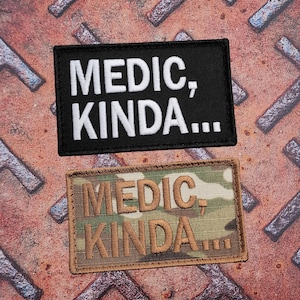 May include: Two rectangular patches with the text "MEDIC, KINDA...". One is black with white lettering, the other is camouflage with brown lettering. These patches are likely for tactical gear or uniforms.