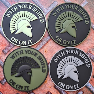 Może przedstawiać: Cztery okrągłe łatki z czarnym tłem i zielonymi, białymi lub szarymi akcentami. Każda łatka przedstawia stylizowane zdjęcie spartanskiego hełmu z pióropuszem i tekstem "WITH YOUR SHIELD OR ON IT".