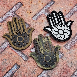 May include: Three hamsa hand charms, one in black, one in camouflage and one in brown. Each charm features a detailed floral design.