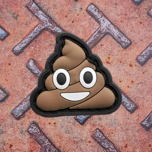 Peut inclure: Un écusson emoji caca marron avec une bordure noire. L'emoji a de grands yeux blancs avec des pupilles noires et une bouche blanche souriante. L'écusson est sur une surface métallique rouillée.