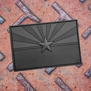 Könnte beinhalten: Ein rechteckiger schwarzer Aufnäher mit dem Design der Arizona-Staatsflagge. Die Flagge zeigt einen Stern und Sonnenstrahlen. Der Aufnäher ist wahrscheinlich aus strapazierfähigem Material gefertigt und zum Anbringen an Kleidung oder Ausrüstung bestimmt.