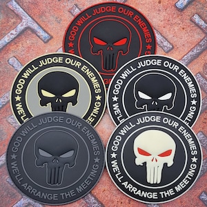 Può includere: Cinque toppe ricamate in bianco e nero con un design a teschio e ossa incrociate. Le toppe hanno un cerchio bianco con testo nero che recita "God Will Judge Our Enemies We'll Arrange The Meeting".