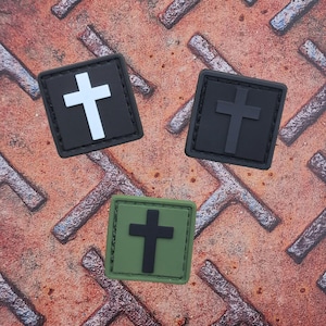 Könnte beinhalten: Drei unterschiedlich farbige Patches mit einem weißen Kreuz auf einem schwarzen Patch, einem schwarzen Kreuz auf einem schwarzen Patch und einem schwarzen Kreuz auf einem grünen Patch.
