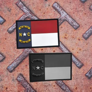 Op de afbeelding: Twee rechthoekige patches met de vlag van de staat North Carolina. Eén patch toont het rood, wit en blauwe ontwerp van de vlag met de tekst "MAY 20th 1775" en "APRIL 12th 1776". De andere patch is in grijstinten.