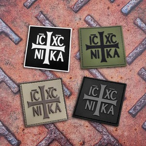 Può includere: Quattro toppe quadrate con un disegno a croce e la scritta "IC XC NIKA". Le toppe sono nere, verde oliva, beige e grigio scuro. Sono su una superficie metallica arrugginita.