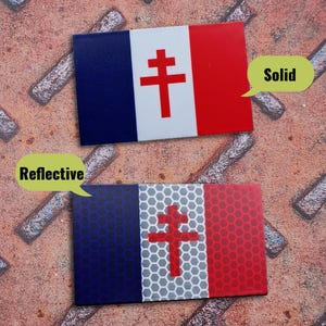 May include: Two rectangular patches featuring the French flag with a red Cross of Lorraine in the center. The top patch has a solid finish, while the bottom patch features a reflective honeycomb pattern. Each patch includes a speech bubble label.