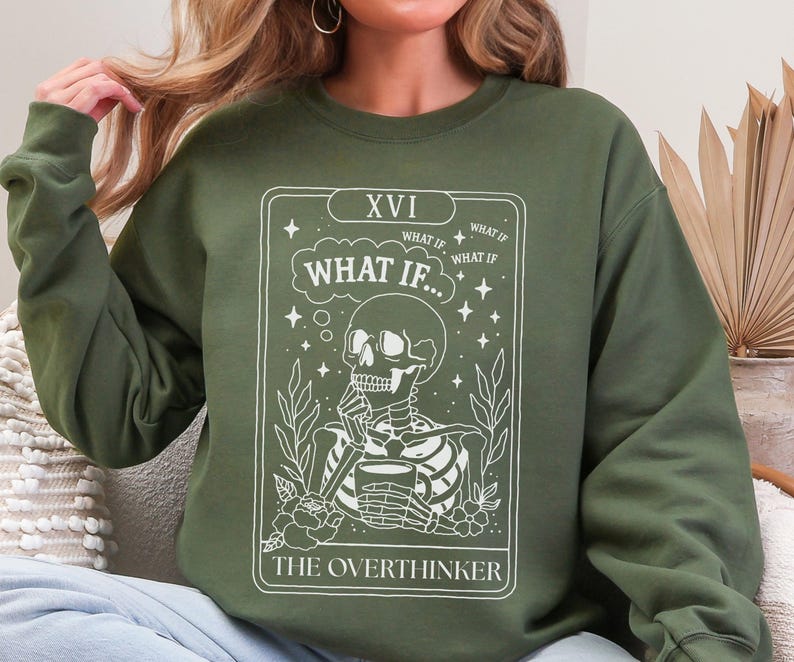 Puede incluir: Sudadera verde oliva con un dise&ntilde;o blanco de un esqueleto sosteniendo una taza, con el texto "WHAT IF..." y "THE OVERTHINKER". El dise&ntilde;o se asemeja a una carta del tarot, con detalles florales y estrellas.