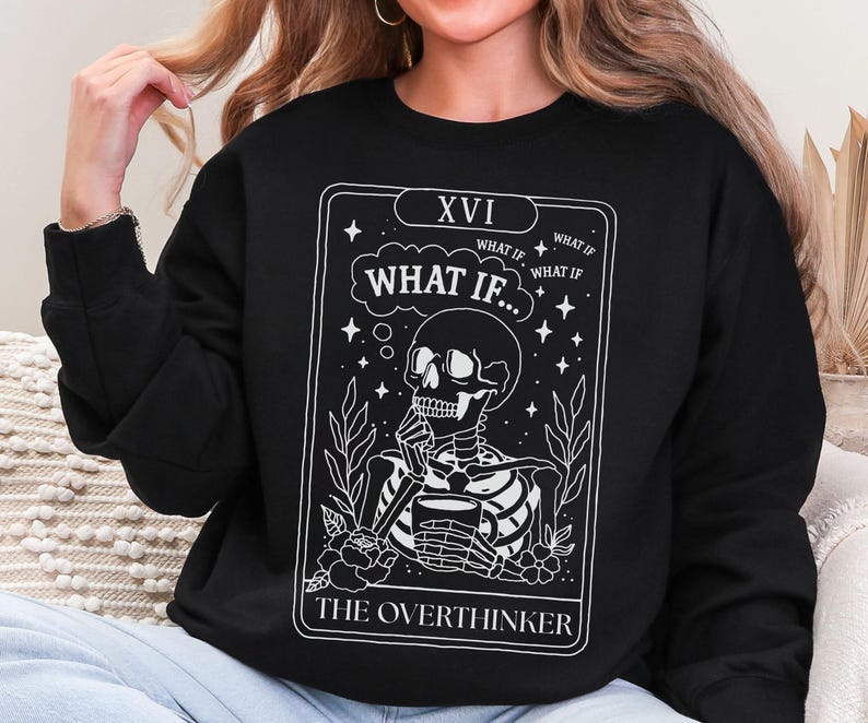 Puede incluir: Sudadera negra con un dise&ntilde;o de carta de tarot blanco. El gr&aacute;fico muestra un esqueleto sosteniendo una taza, con el texto "WHAT IF..." y "THE OVERTHINKER". El dise&ntilde;o incluye estrellas, hojas y el n&uacute;mero romano XVI.