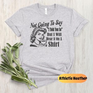 May include: Gray t-shirt with a retro illustration of a woman holding a cup of coffee. The text on the shirt reads "Not Going To Say "I Told You So" But I Will Wear it On A Shirt".