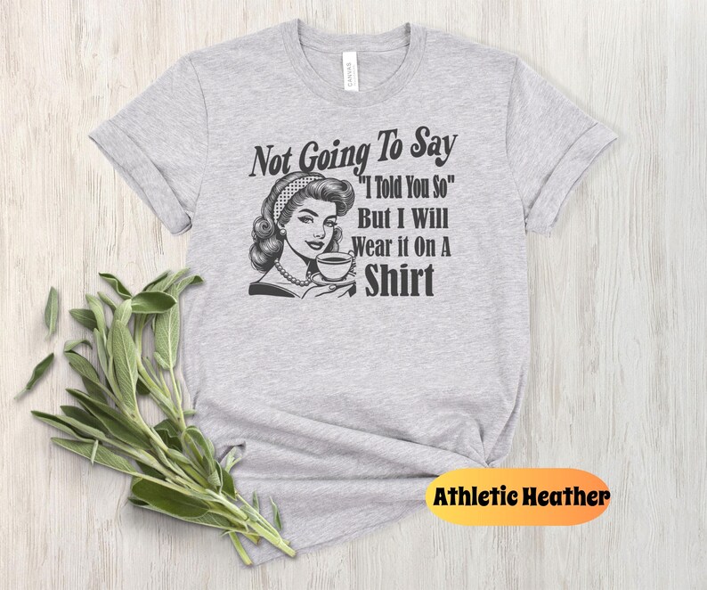 May include: Gray t-shirt with a retro illustration of a woman holding a cup of coffee. The text on the shirt reads "Not Going To Say "I Told You So" But I Will Wear it On A Shirt".