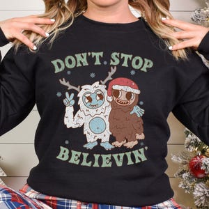May include: Black sweatshirt with a white and green graphic of two cartoon monsters. The text "Don't Stop Believin'" is printed on the sweatshirt.