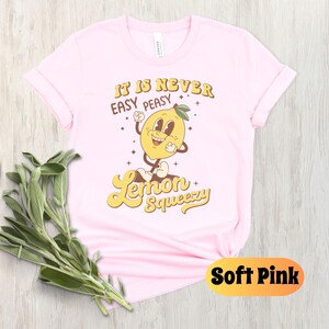 May include: A pink t-shirt with a yellow lemon cartoon character and the text "It is never easy peasy Lemon Squeezy".