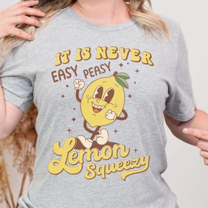 May include: Gray t-shirt with a cartoon lemon graphic and the text "It is never easy peasy Lemon Squeezy".