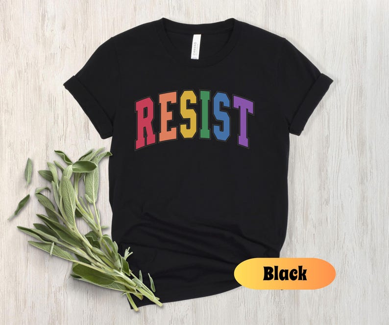 May include: Black t-shirt with the word "RESIST" in rainbow colors. The word is in a collegiate font.