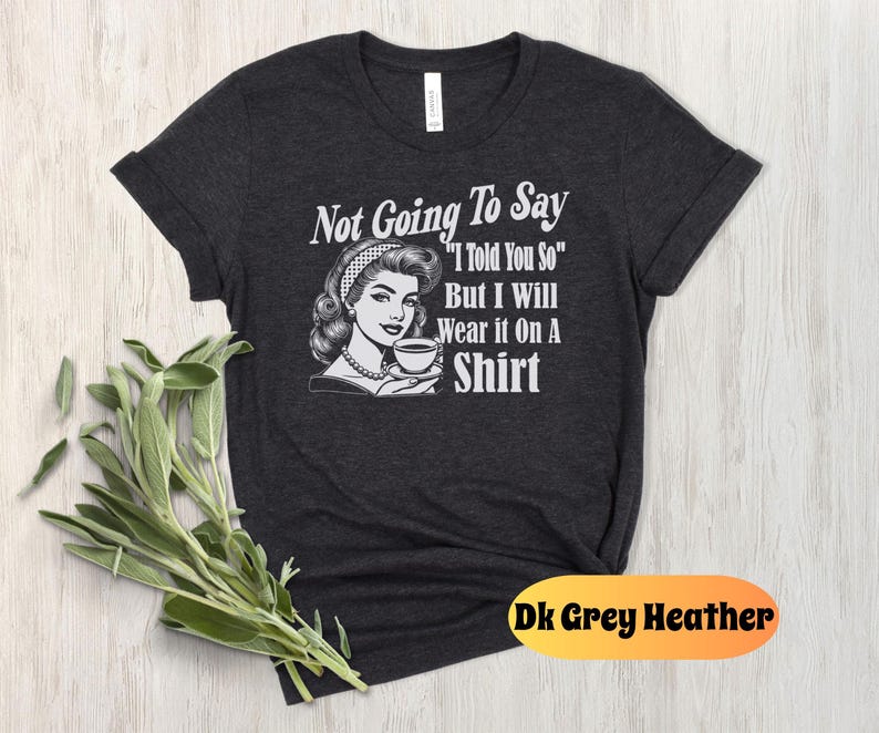 May include: Dark grey heather t-shirt with a retro illustration of a woman holding a cup of coffee. The text "Not Going To Say "I Told You So" But I Will Wear it On A Shirt" is printed on the shirt.