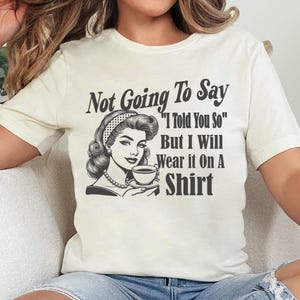 May include: White t-shirt with a black and white illustration of a woman holding a cup of coffee. The text on the shirt reads "Not Going To Say "I Told You So" But I Will Wear it On A Shirt"