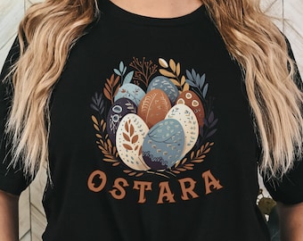 May include: Black t-shirt with a colorful illustration of eggs and floral designs. The text "OSTARA" is printed below the illustration.