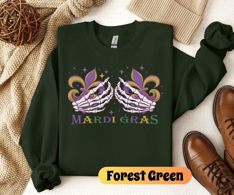 May include: Forest green sweatshirt with a Mardi Gras design featuring two skeletal hands holding fleur-de-lis. The text "Mardi Gras" is printed in yellow and green.