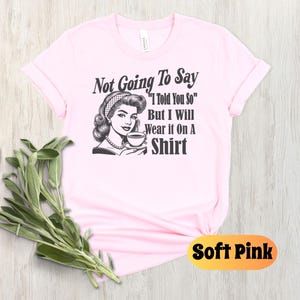 May include: A pink t-shirt with a black and white illustration of a woman holding a cup. The text on the shirt reads "Not Going To Say "I Told You So" But I Will Wear it On A Shirt".