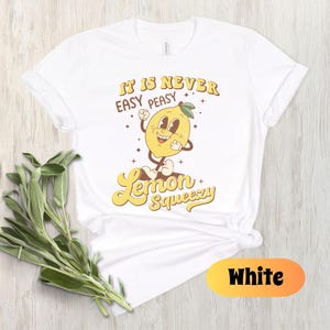 May include: White t-shirt with a yellow lemon graphic and the text "It is never easy peasy Lemon Squeezy".
