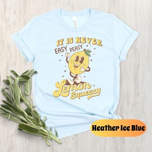 May include: Light blue t-shirt with a cartoon lemon graphic and the text "It is never easy peasy lemon squeezy".