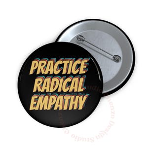 May include: A black button with the text "PRACTICE RADICAL EMPATHY" in yellow, red, and blue. The button is round with a metal pin back. Another button is visible in the background.