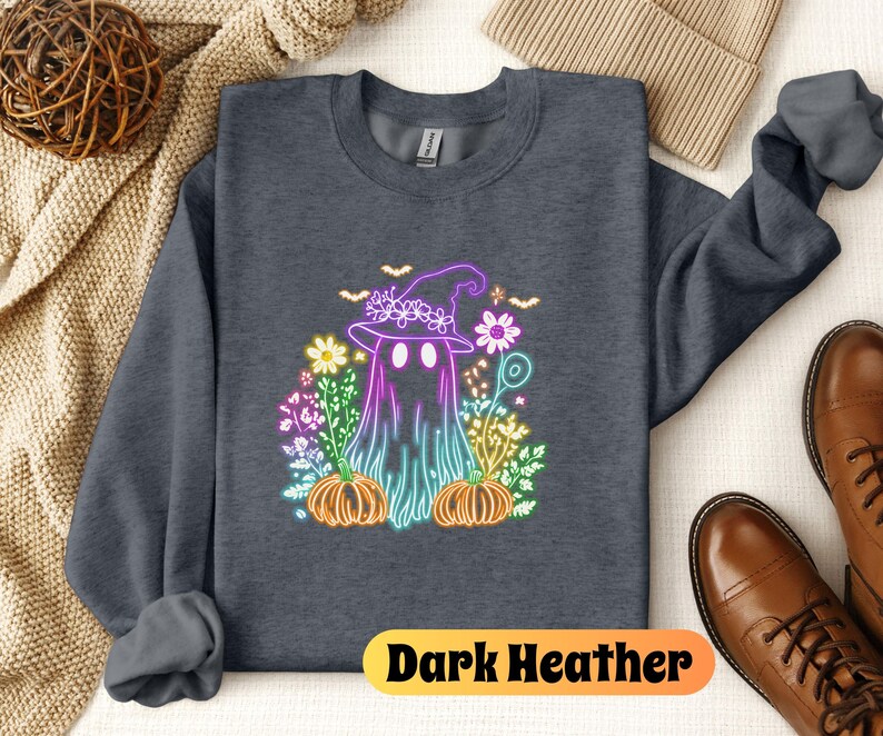 K&ouml;nnte beinhalten: Dunkelgrauer Sweatshirt mit einem Neon-Regenbogen-Motiv eines Geistes, der einen Hexenhut tr&auml;gt und von Blumen und K&uuml;rbissen umgeben ist. Der Text "Dark Heather" ist unten auf dem Sweatshirt aufgedruckt.
