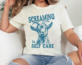 May include: A white t-shirt with a blue graphic of a goat and the text "Screaming is Self Care".