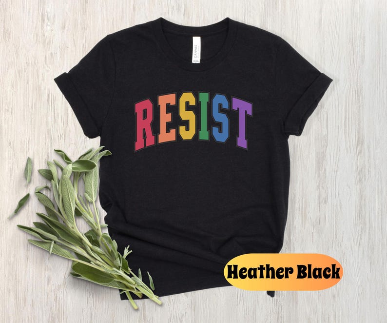 May include: Black t-shirt with the word "RESIST" in rainbow colors. The word is in a collegiate font style.