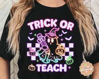 May include: Black t-shirt with a neon pink, green, and blue graphic of a ghost wearing a witch hat and holding a pencil. The text "Trick or Teach" is written in white letters.