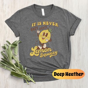 May include: A dark heather grey t-shirt with a retro cartoon lemon graphic and the text "It is never easy peasy Lemon Squeezy".