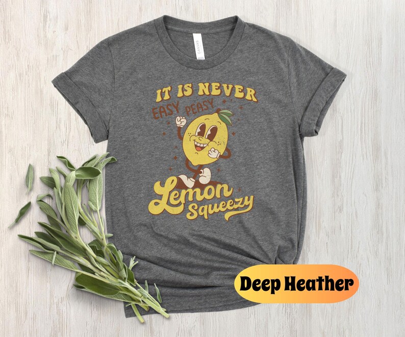 May include: A dark heather grey t-shirt with a retro cartoon lemon graphic and the text "It is never easy peasy Lemon Squeezy".