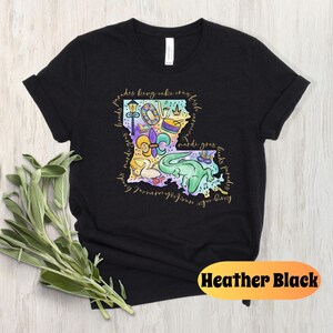 Op de afbeelding: Zwart T-shirt met een kleurrijke illustratie van de staat Louisiana. De illustratie bevat Mardi Gras-parels, een koningentaart, een fleur-de-lis, een trommel, een paradewagen en een alligator. De tekst "parades king cake crawfish first friday mardi gras floats parades" staat rond de omtrek van de staat.