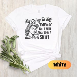 May include: White t-shirt with a black and white illustration of a woman holding a cup of coffee. The text on the shirt reads "Not Going To Say "I Told You So" But I Will Wear it On A Shirt"