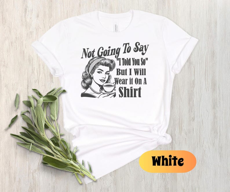 May include: White t-shirt with a black and white illustration of a woman holding a cup of coffee. The text on the shirt reads "Not Going To Say "I Told You So" But I Will Wear it On A Shirt"