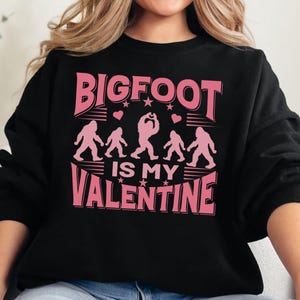 May include: Black sweatshirt with a pink graphic print that says "BIGFOOT IS MY VALENTINE". The graphic features a silhouette of Bigfoot and hearts.