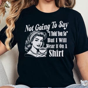 May include: Black t-shirt with a white graphic of a woman holding a cup of coffee. The text on the shirt reads "Not Going To Say "I Told You So" But I Will Wear it On A Shirt"