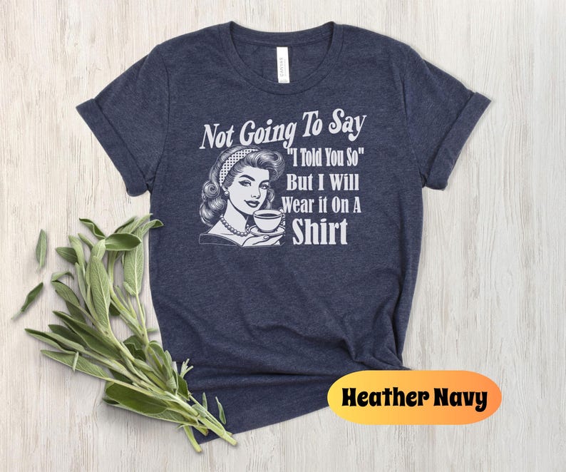 May include: A navy blue t-shirt with a retro-style illustration of a woman holding a cup of coffee. The text on the shirt reads "Not Going To Say "I Told You So" But I Will Wear It On A Shirt".