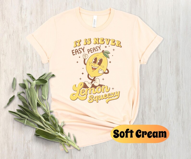 May include: A soft cream colored t-shirt with a retro cartoon lemon graphic and the text "It is never easy peasy Lemon Squeezy".