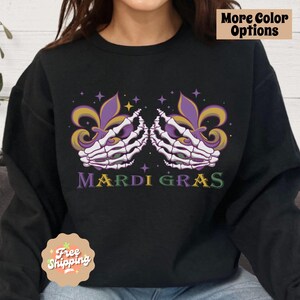 May include: Black sweatshirt with a purple and gold Mardi Gras design featuring two skeletal hands holding a fleur-de-lis. The text "Mardi Gras" is printed below the design.