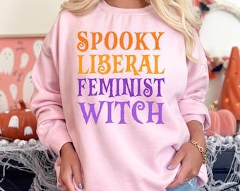 May include: Pink sweatshirt with the text "Spooky Liberal Feminist Witch" in orange and purple.