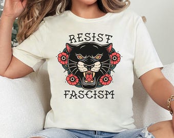 Könnte beinhalten: Weißes T-Shirt mit einem schwarzen Panther-Motiv und dem Text "Resist Fascism" in schwarzen Buchstaben. Der Panther ist von roten Blumen umgeben.