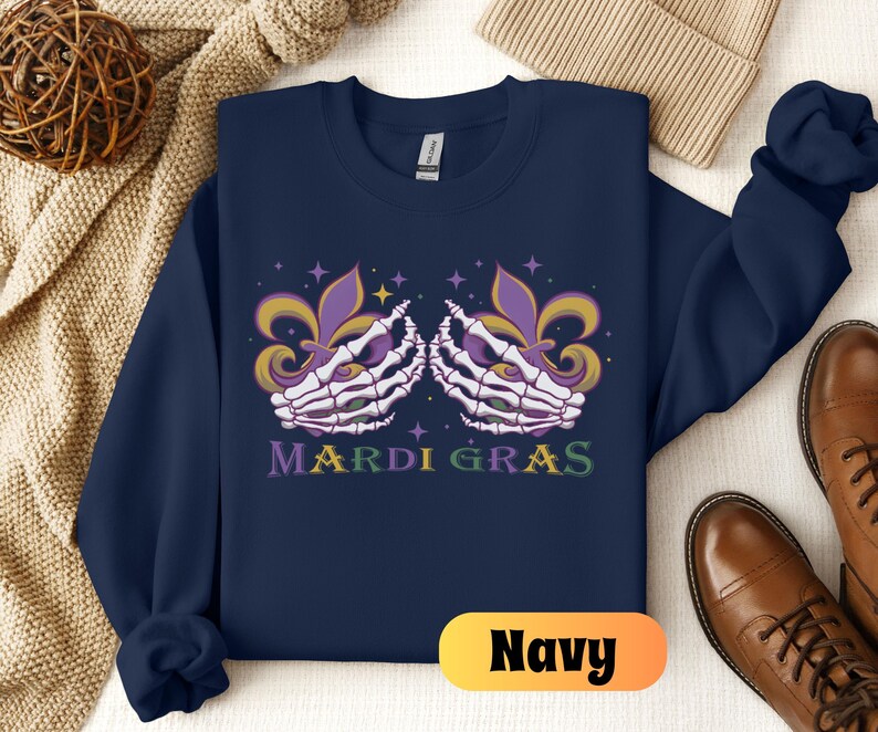 May include: Navy blue sweatshirt with a Mardi Gras design featuring two skeletal hands holding purple, green, and gold fleur-de-lis. The text "Mardi Gras" is printed below the hands.