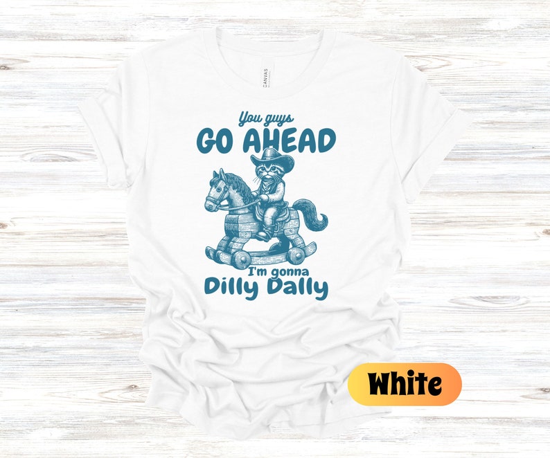 May include: White t-shirt with a blue graphic of a cat riding a rocking horse. The text on the shirt reads "You guys go ahead I'm gonna dilly dally."