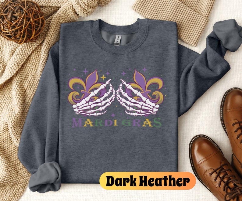 May include: Dark heather grey sweatshirt with a graphic of two skeletal hands holding purple and gold fleur-de-lis. The text "Mardi Gras" is printed below the hands.