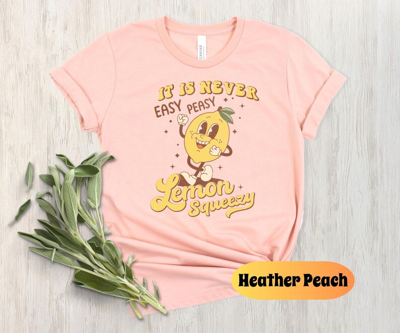May include: A pink t-shirt with a retro-style graphic of a smiling lemon with the text "It is never easy peasy lemon squeezy".
