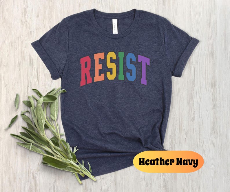 May include: A heather navy blue t-shirt with the word "RESIST" printed in rainbow colors across the front.