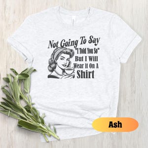 May include: A white t-shirt with a black and white illustration of a woman drinking coffee. The text on the shirt reads "Not Going To Say "I Told You So" But I Will Wear it On A Shirt".