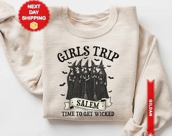 May include: Sand-colored sweatshirt with the text "GIRLS TRIP" above a graphic of five witches in black dresses and hats. Below the graphic, the text reads "SALEM" and "TIME TO GET WICKED". The sweatshirt has long sleeves.